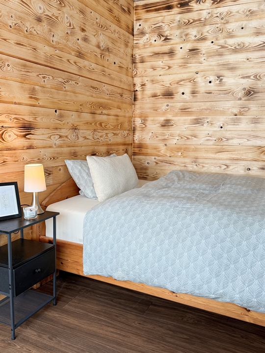 Schlafzimmer mit Holzwand, Bett und Nachttisch