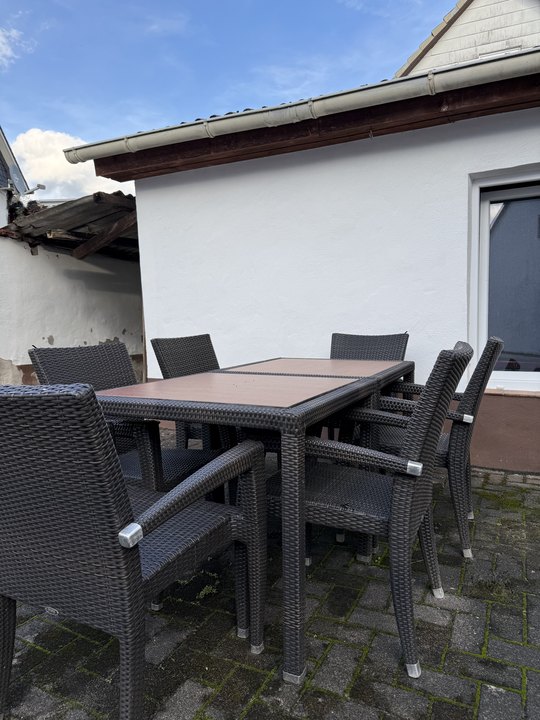 Tisch und Stühle im Freien vor einem weißen Nebengebäude