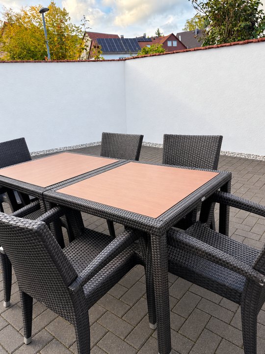 Tisch mit Stühlen auf dem Pflaster im Freien vor einer weißen Mauer
