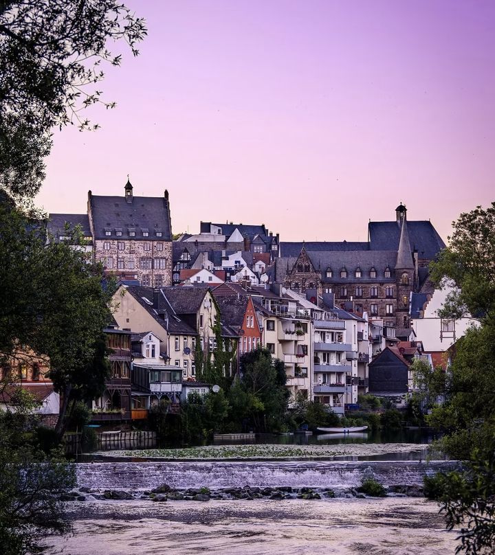 Blick über das Wehr der Lahn auf die Häuser der Marburger Altstadt am Hang im Abendlicht
